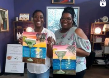 Two women are holding up paintings of margaritas.