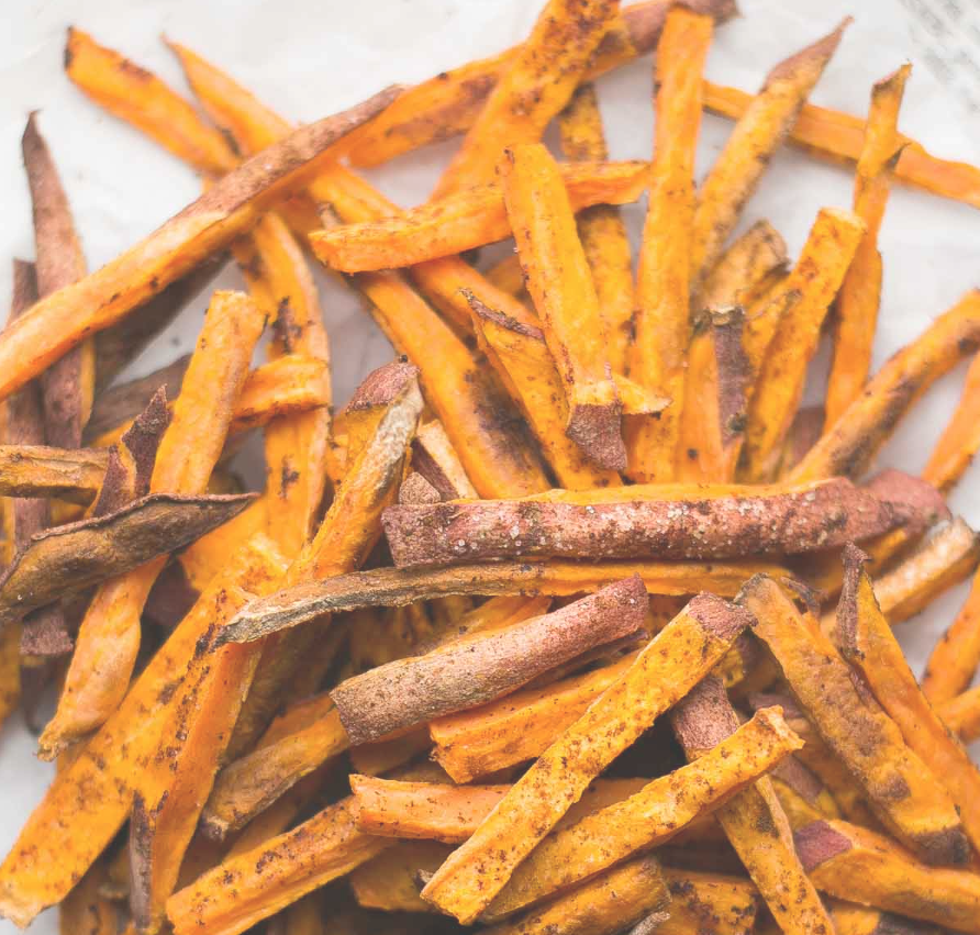 A pile of sweet potato fries on a white paper.