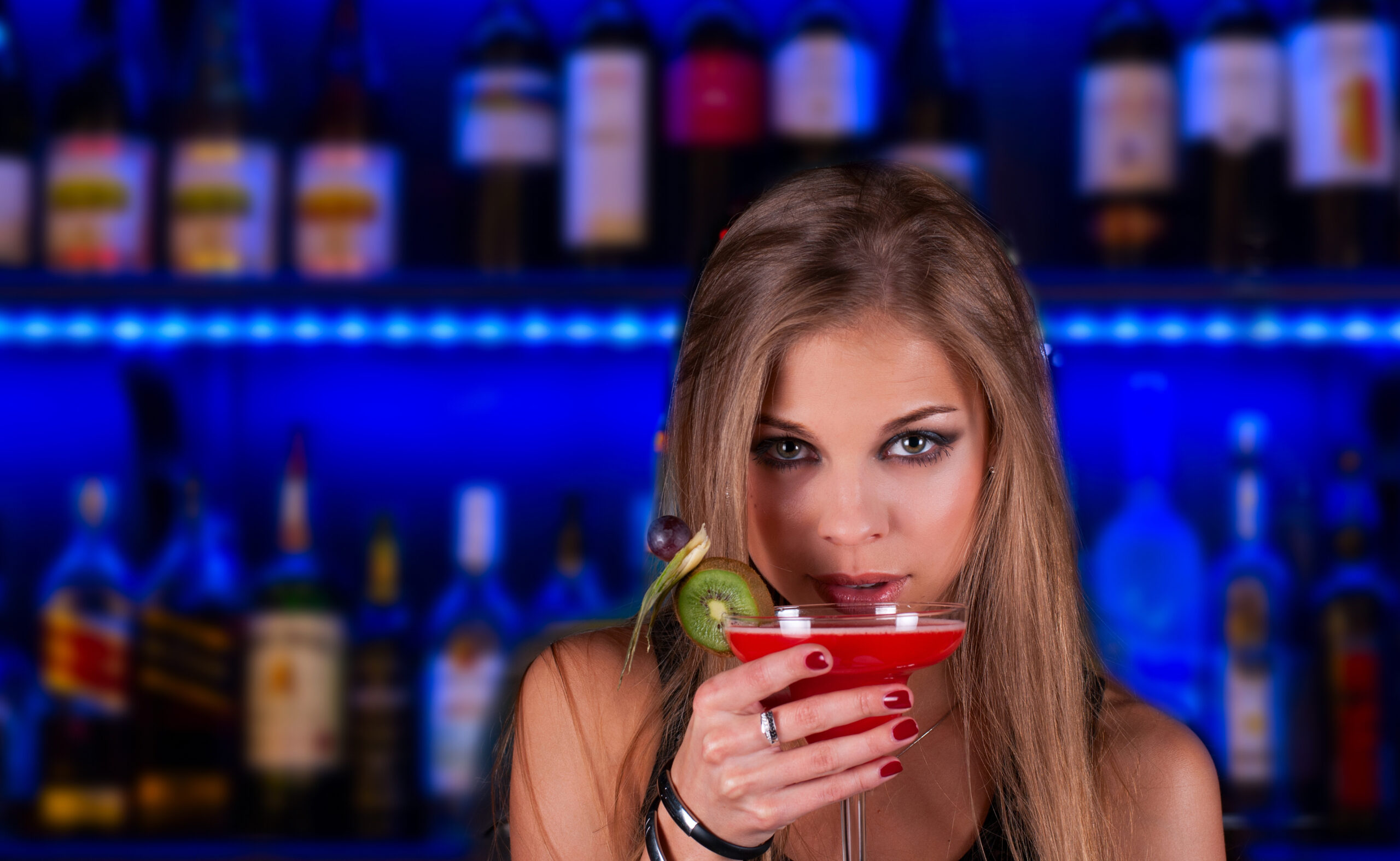 A woman is holding a cocktail in front of a bar.