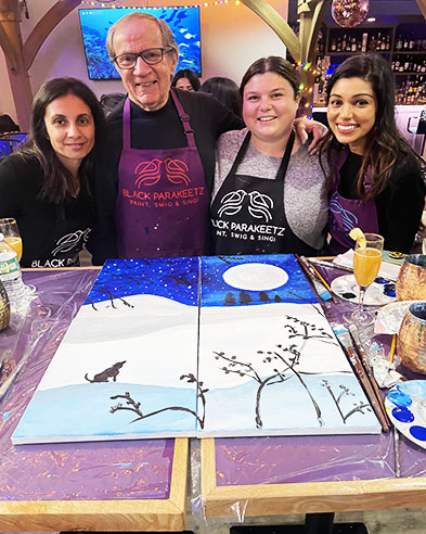 Four guests in Black Parakeetz aprons smiling behind their connected canvas painting