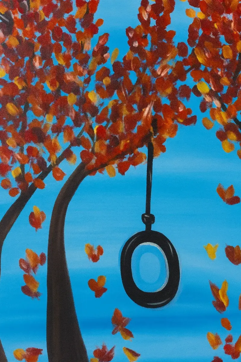 A tire swing hangs from a tree with autumn leaves against a blue sky.